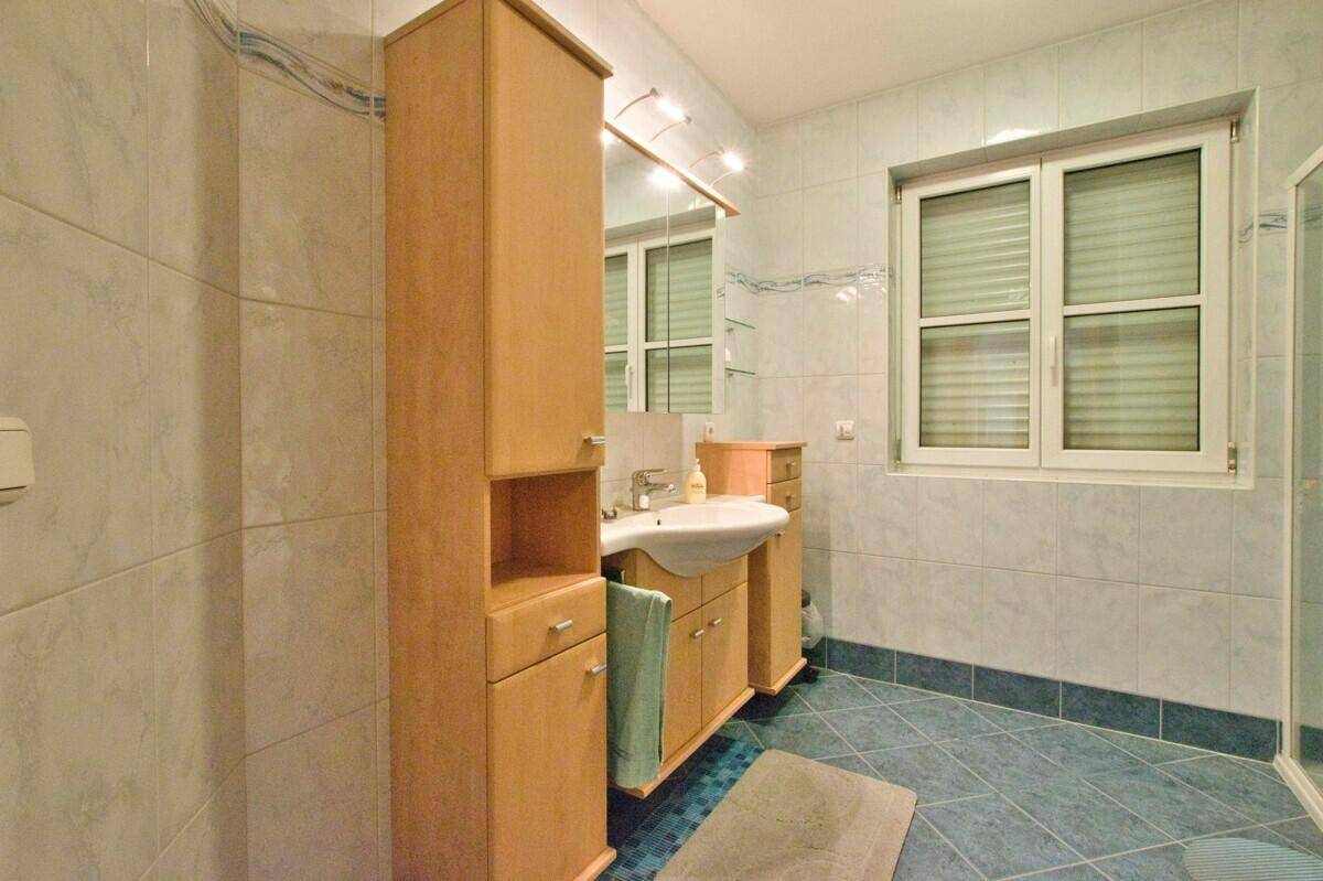 Badezimmer mit Einzelwaschbecken, Holzschränken und hellblauen Fliesen, inklusive Fenster.