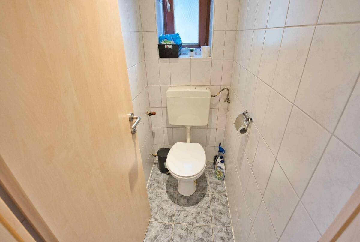 Separate Toilette mit Fenster und hellen Wand- und Bodenfliesen, praktisch für Gäste.