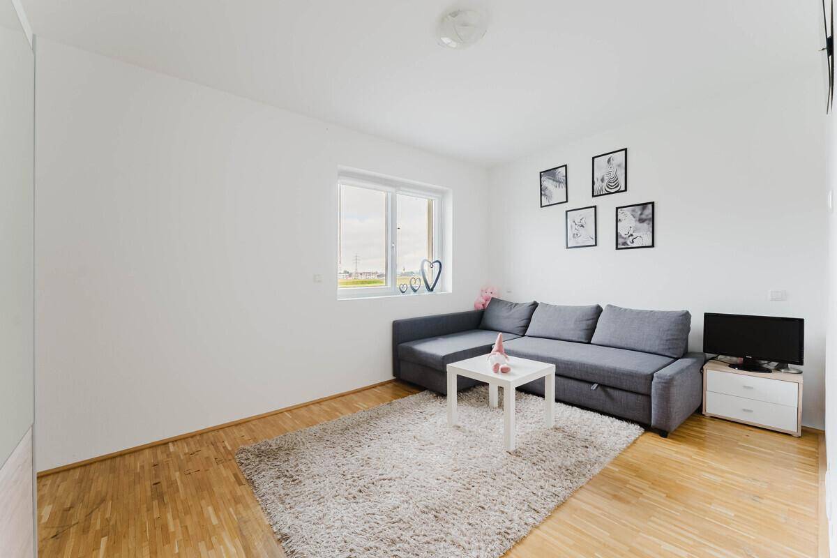 Helles Zimmer mit Sofa, Holzboden und Fenster, ideal als Gäste- oder Kinderzimmer.