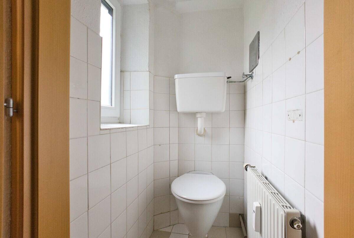 Kleines WC mit Fenster und weißen Fliesen, einfach und funktional ausgestattet.