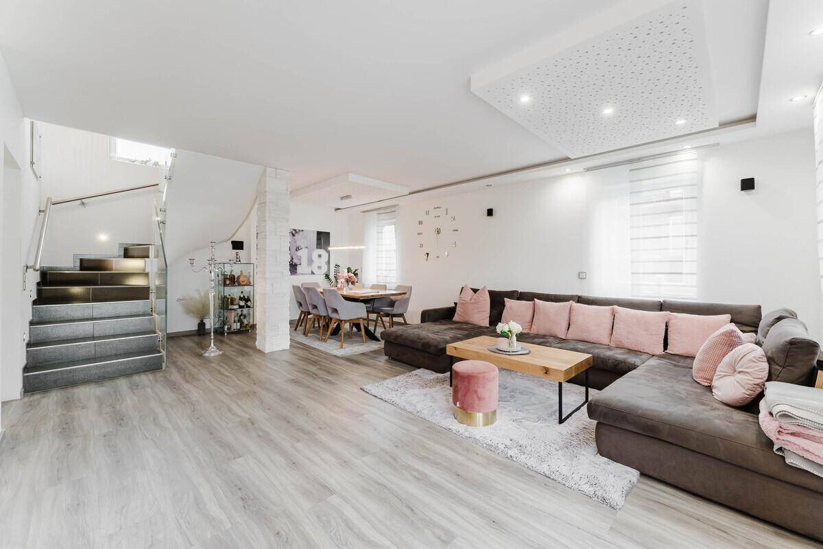 Heller Wohn-Essbereich mit großem Ecksofa, stilvoller Einrichtung und moderner Treppe.