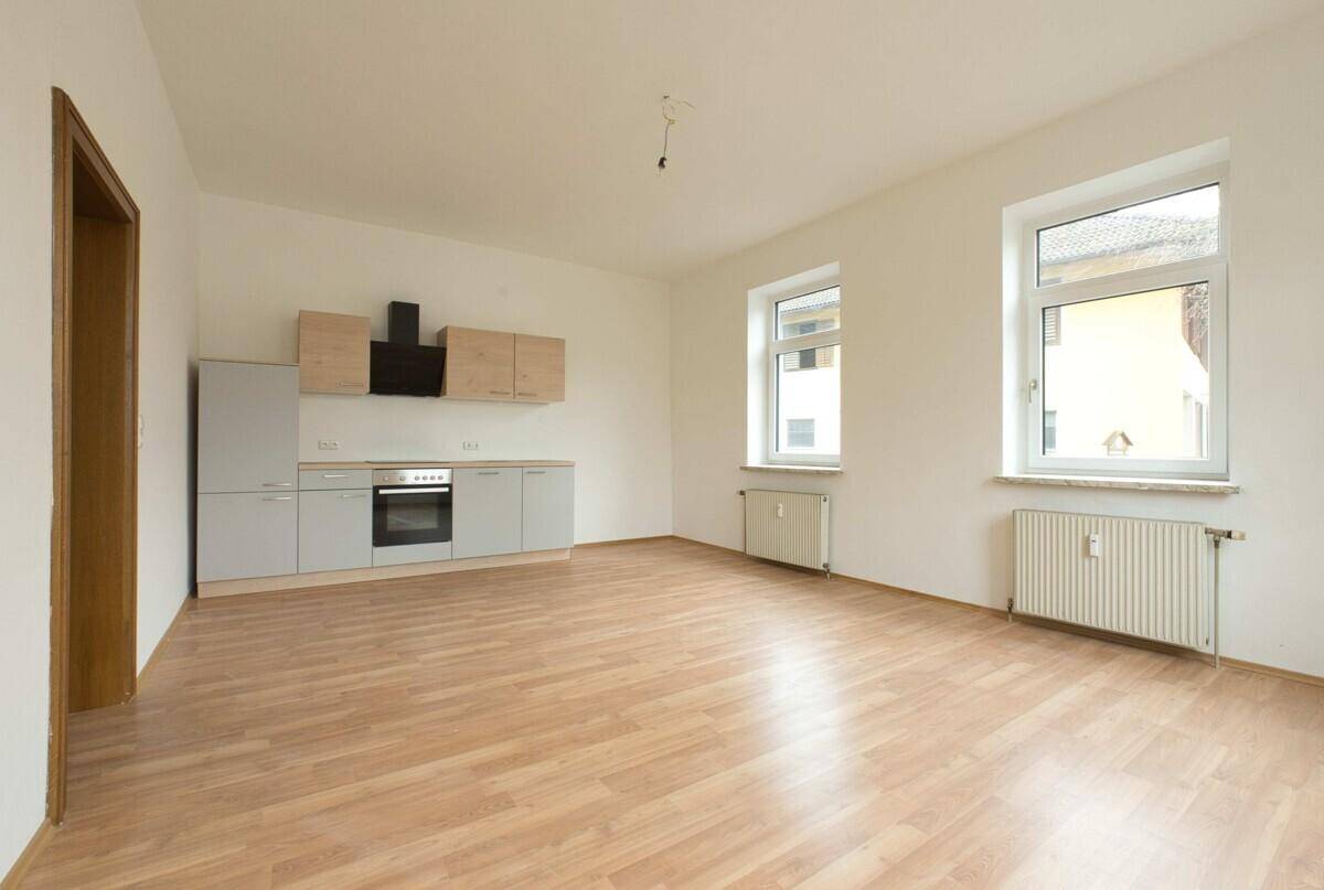 Helle Küche mit Laminatboden, Einbauküche und zwei Fenstern, bereit zur individuellen Gestaltung.