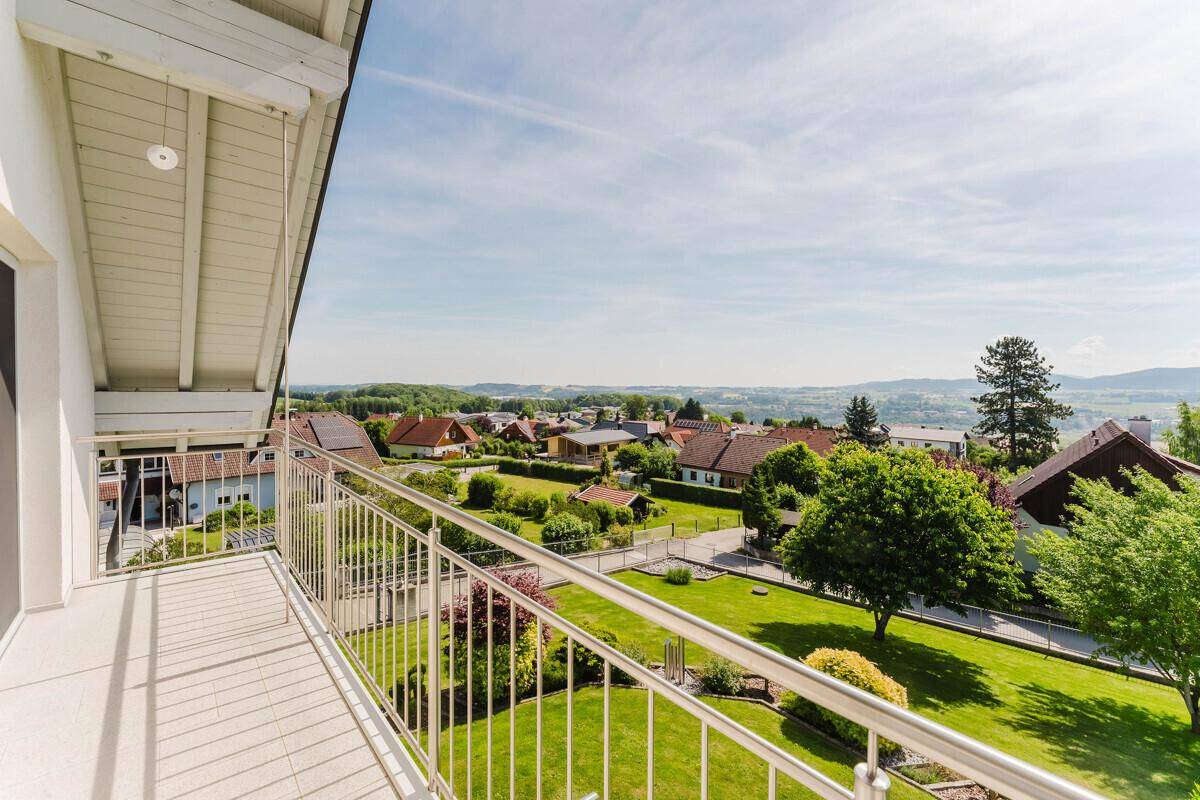 Sonniger Balkon mit weitem Blick über die grüne Landschaft und die umliegenden Häuser.