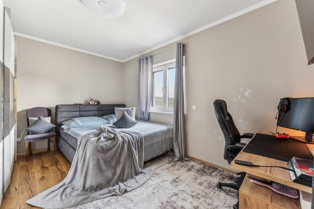 Modernes Schlafzimmer mit Holzboden, Schreibtisch und Blick ins Grüne.