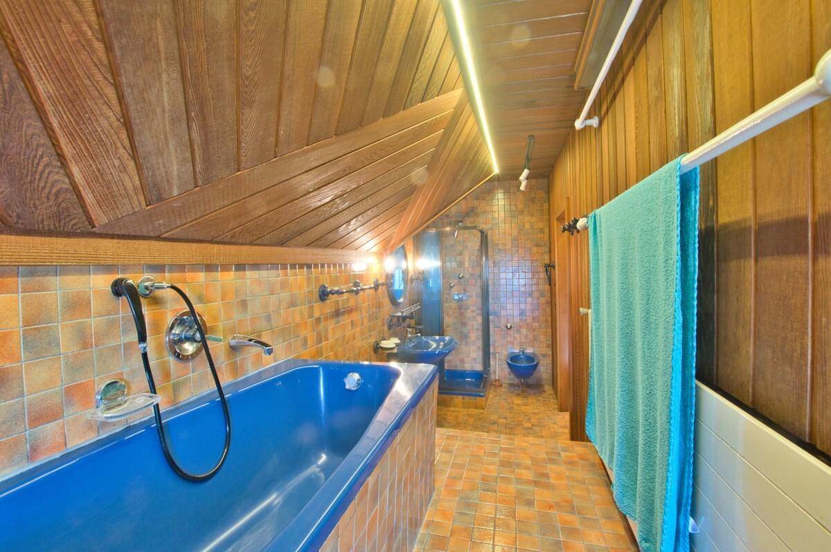 Badezimmer im Dachgeschoss mit blauer Badewanne, Bidet und farbigen Fliesen an Wänden und Boden.
