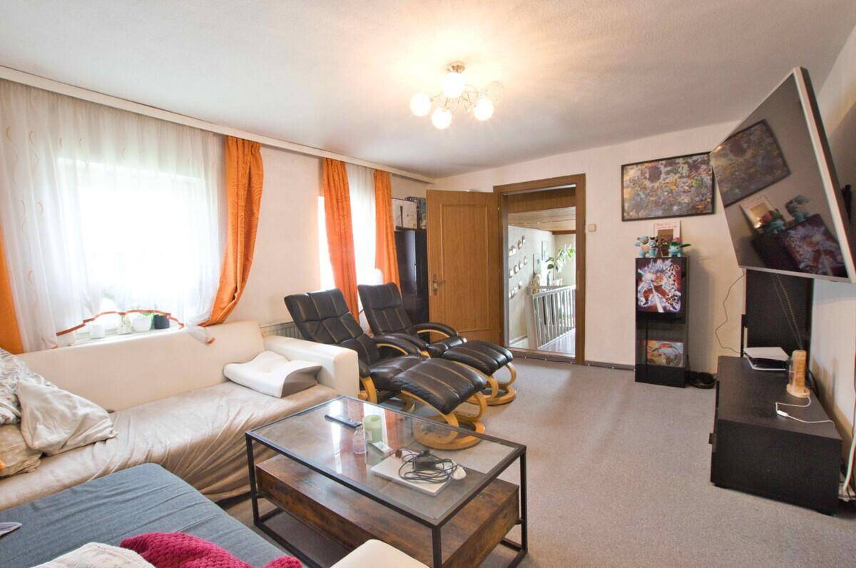 Helles Wohnzimmer mit bequemen Sitzmöbeln, Fenstern und orangefarbenen Vorhängen.