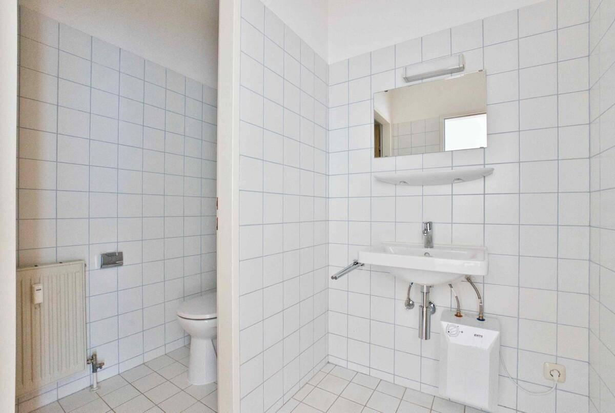 Gefliestes Badezimmer mit Toilette, Waschbecken und einem Spiegel, alles in einem hellen Design.