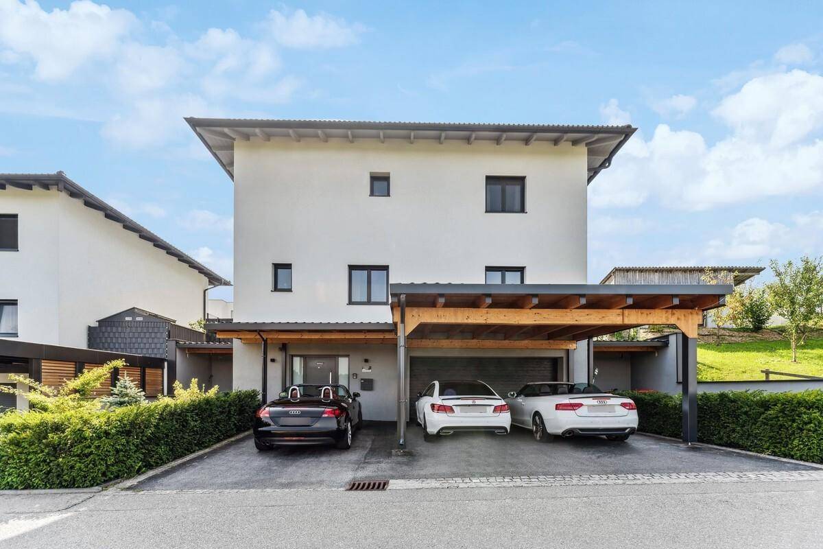 Modernes Einfamilienhaus mit Carport und mehreren Parkplätzen vor dem Eingang.