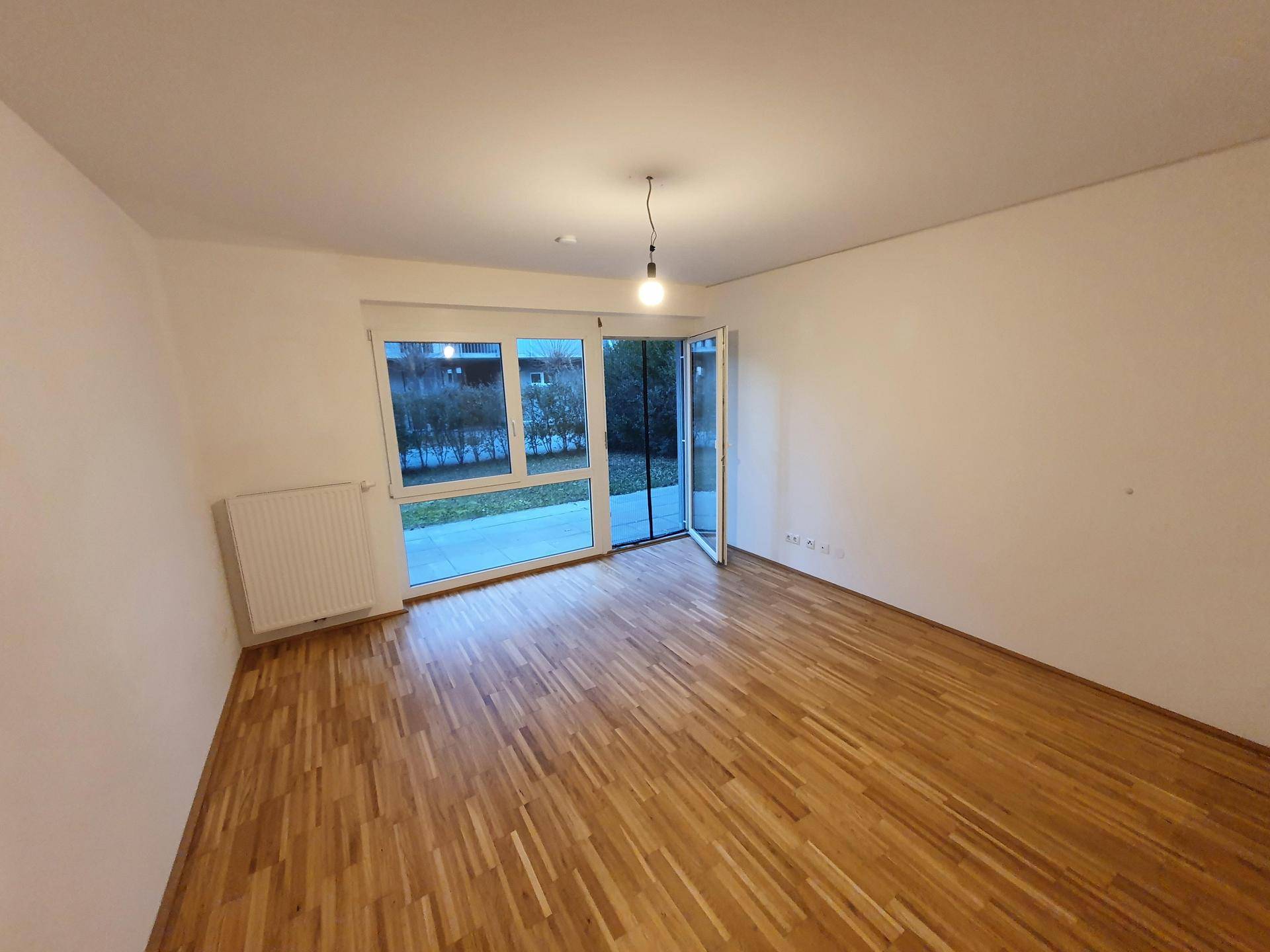 Geräumiges Wohnzimmer mit hellem Parkettboden und Zugang zur Terrasse durch große Fenster.