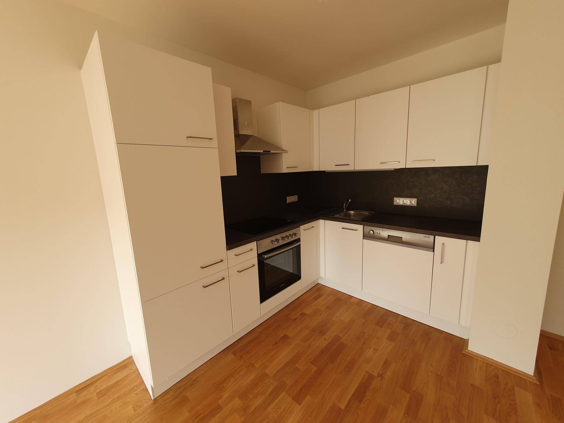 Moderne Küchenzeile mit weißen Schränken, dunkler Arbeitsplatte und integrierten Geräten.