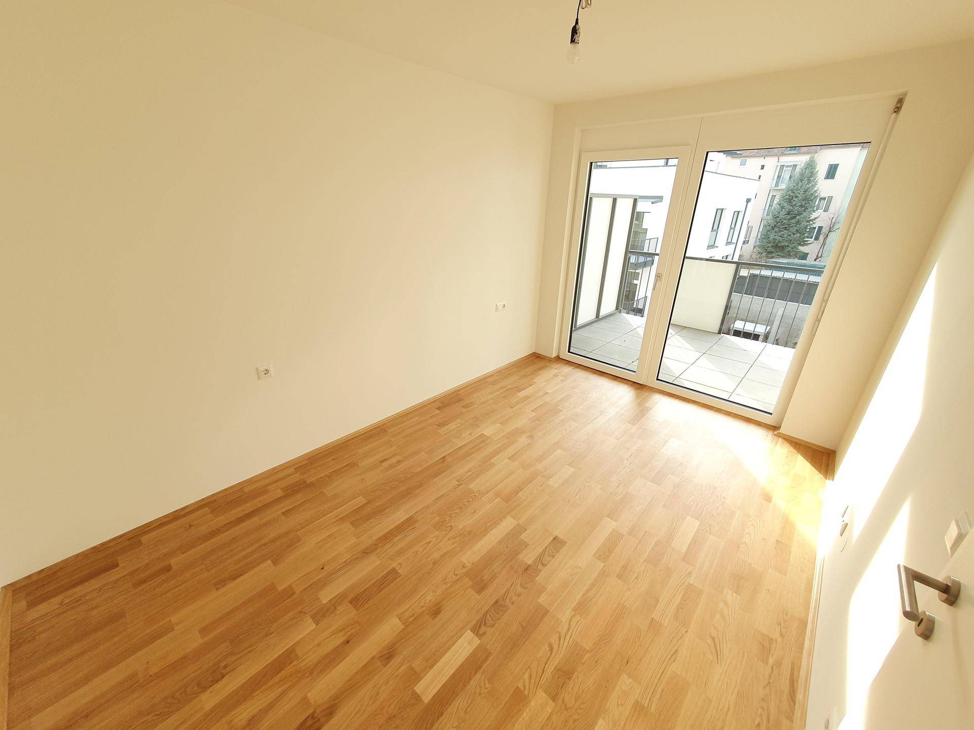 Schlafzimmer mit Holzboden, großen Fenstern und direktem Zugang zum Balkon.