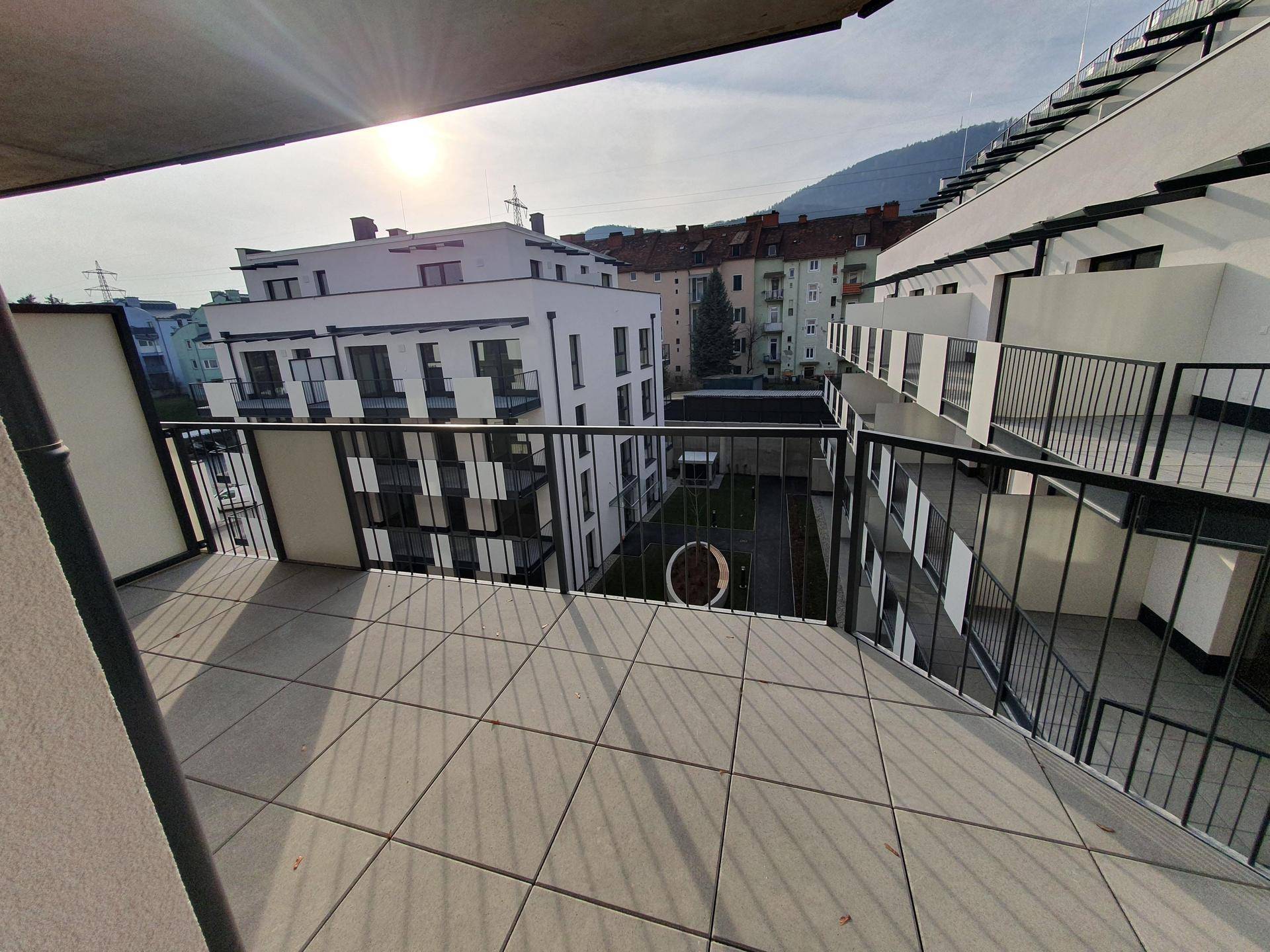 Geräumiger Balkon mit Fliesenboden und Blick auf den grünen Innenhof der Wohnanlage.