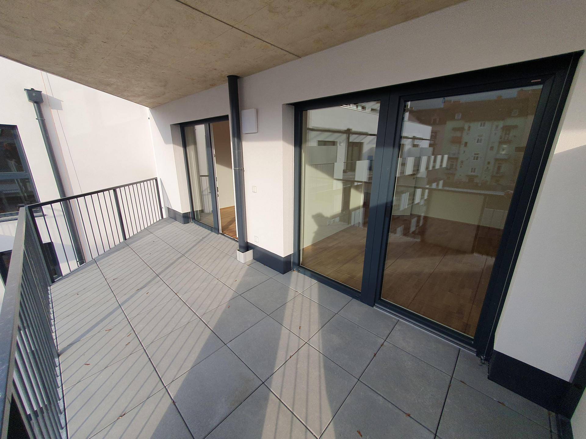 Breiter Balkon mit Fliesenboden und Blick auf die umliegenden modernen Gebäude.