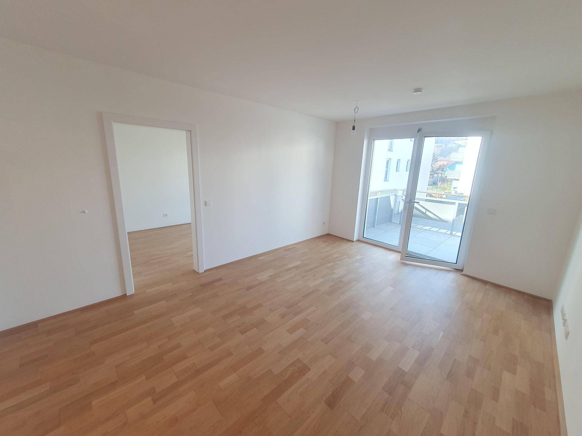 Helles Wohnzimmer mit Parkettboden und Zugang zu einem großen Balkon.