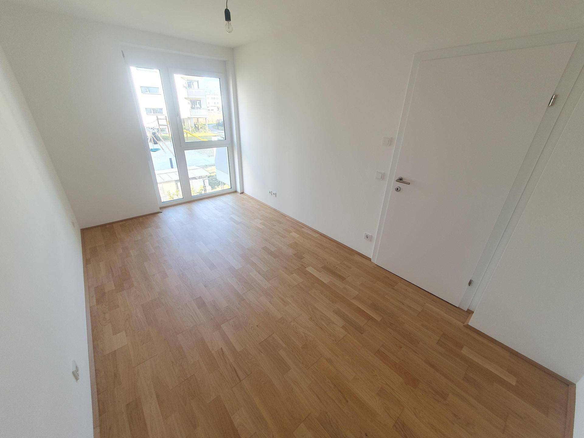 Helles Schlafzimmer mit Parkettboden und großem Fenster für viel Tageslicht.