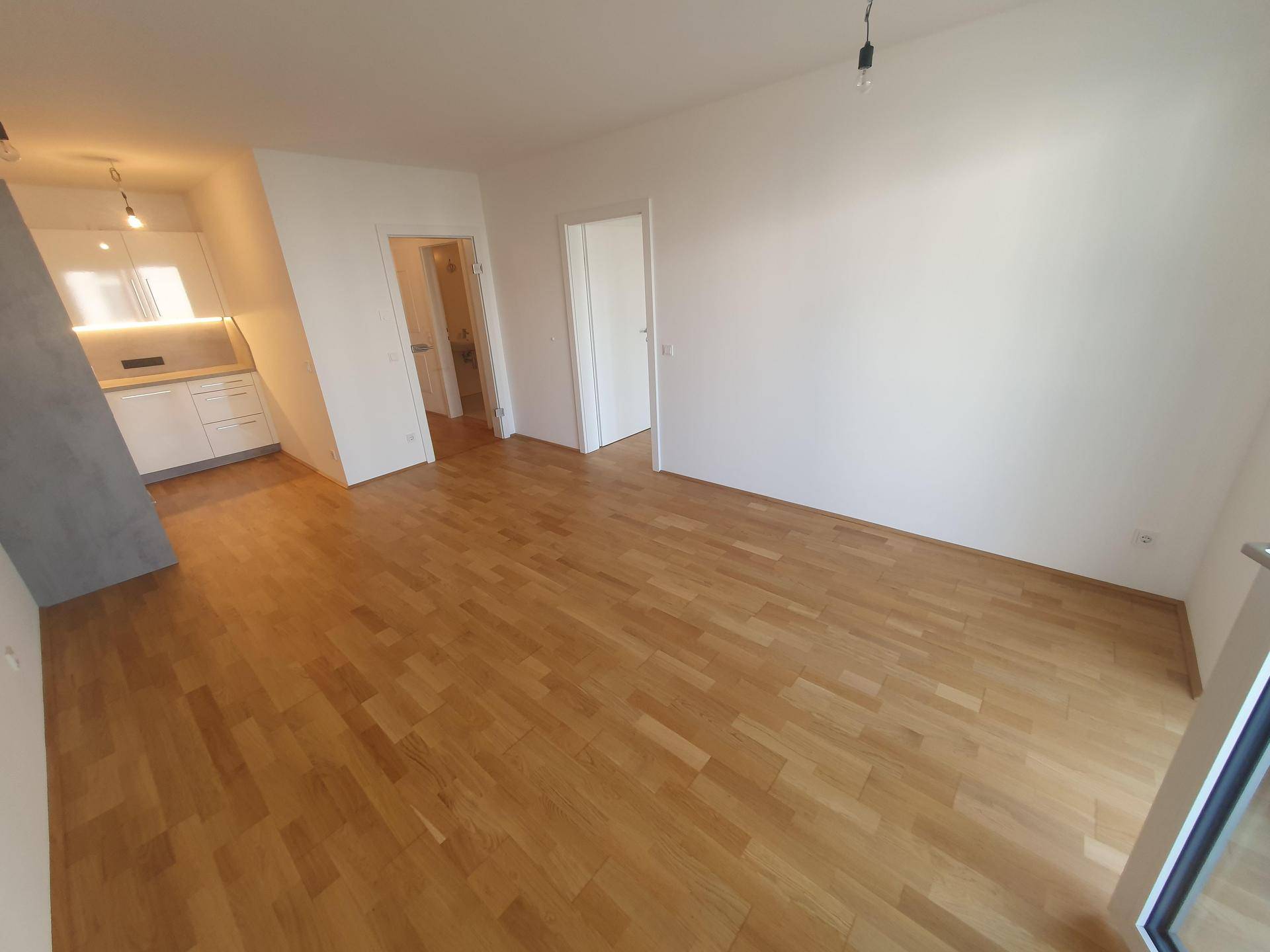 Geräumiger Wohnbereich mit Parkettboden und Blick auf die integrierte Küchenzeile.