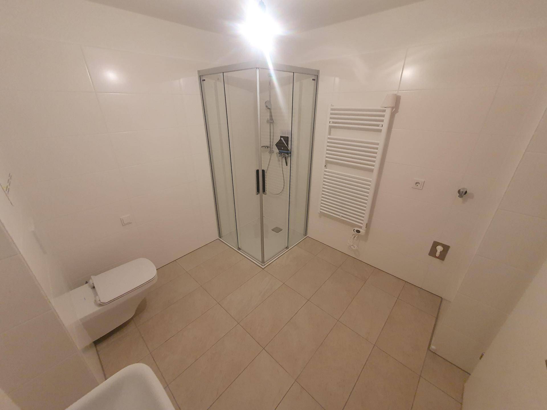Helles Badezimmer mit Duschkabine, WC und praktischem Handtuchheizkörper.