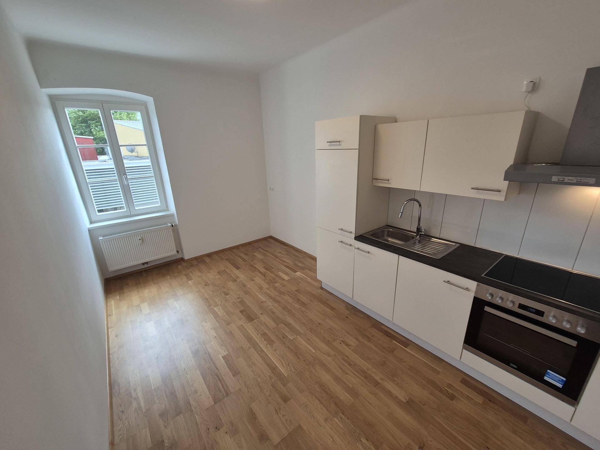 Kleine, moderne Küchenzeile mit weißen Schränken, integriertem Backofen und Holzparkettboden.