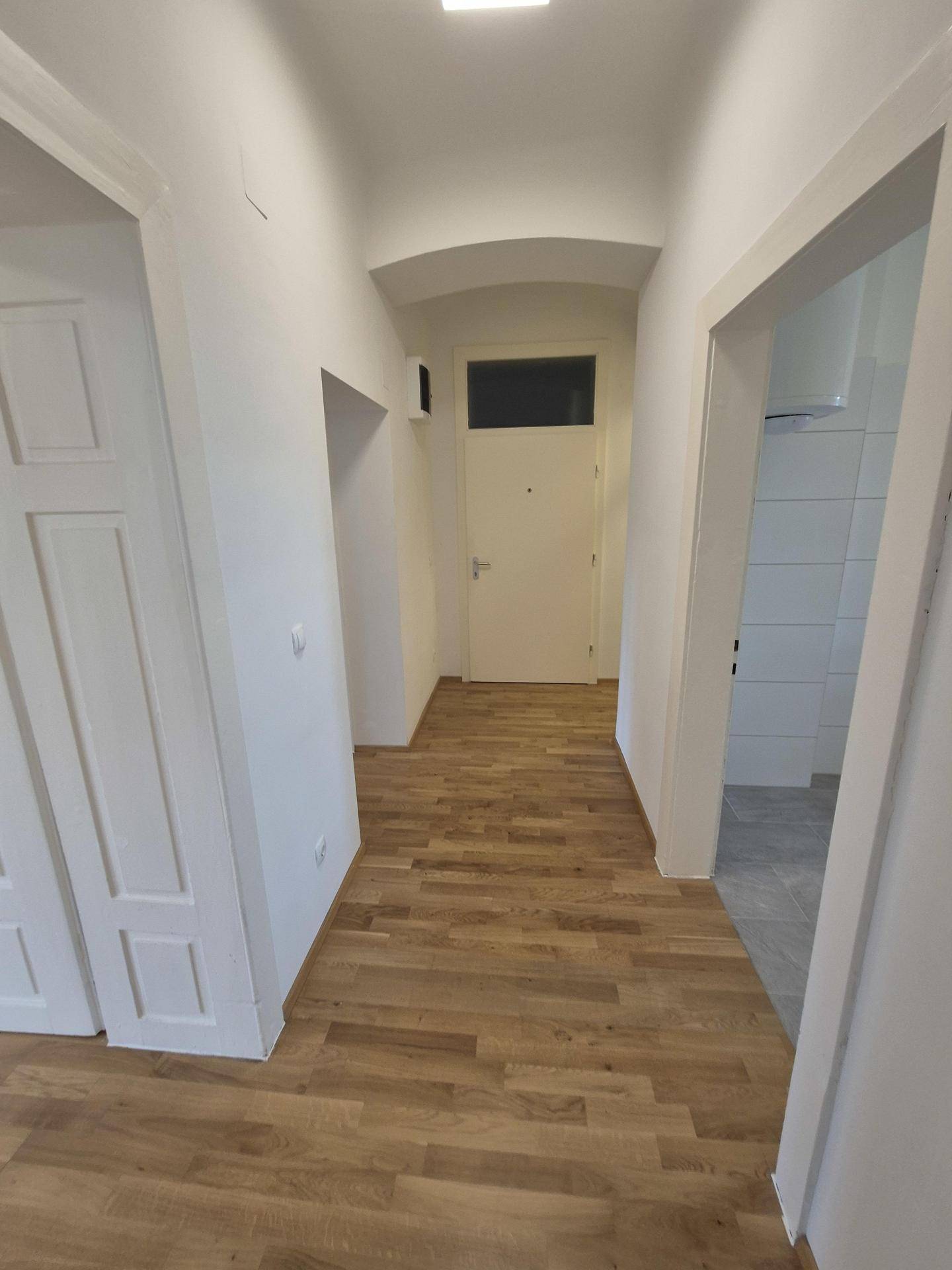 Heller Flur mit Holzparkettboden, weißen Wänden und Zugang zu verschiedenen Räumen.