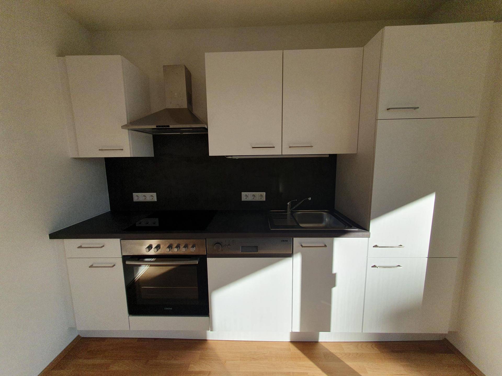 Moderne Einbauküche mit weißen Schränken, schwarzer Arbeitsplatte und integrierten Geräten.