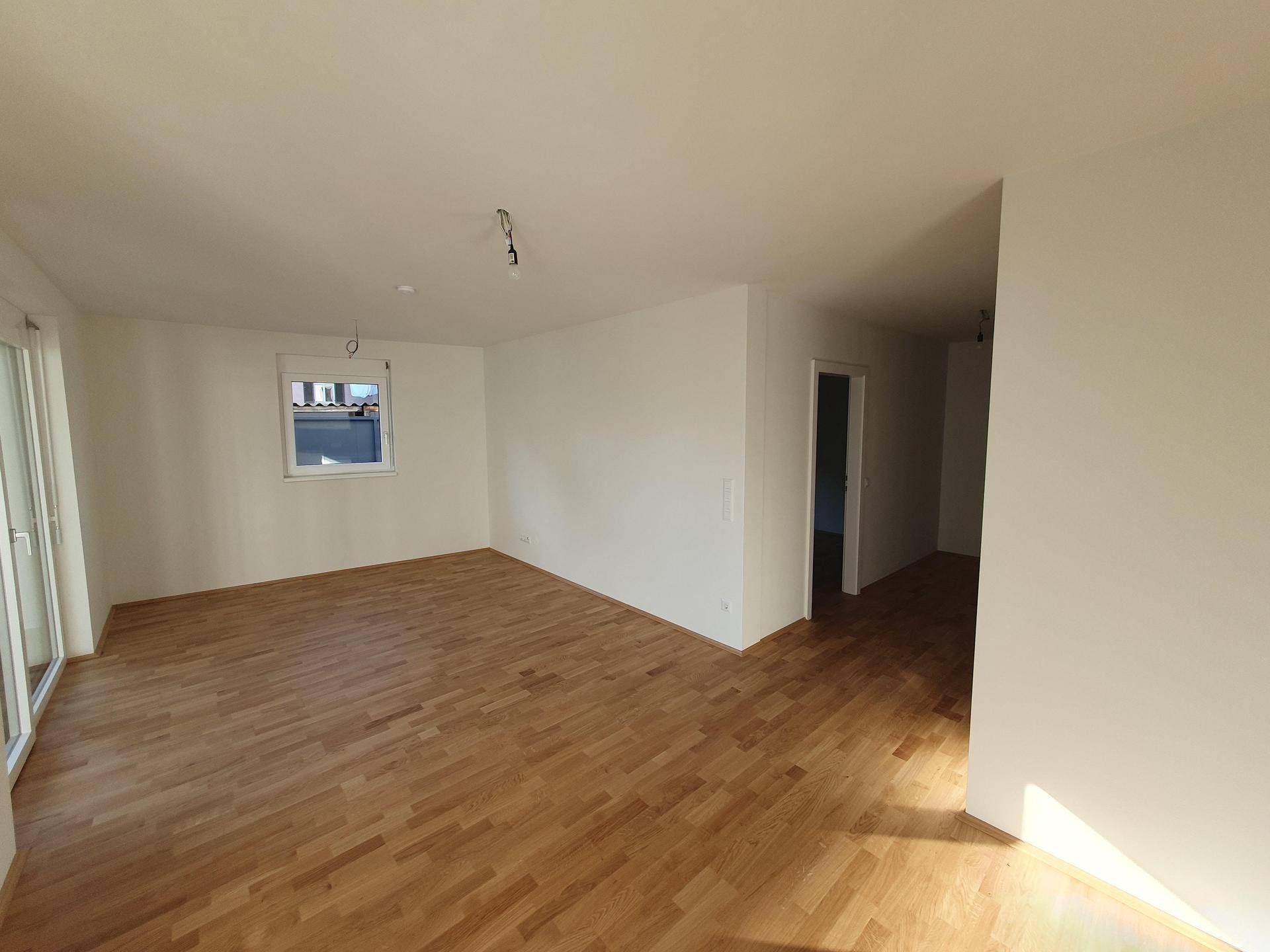 Geräumiger Wohnbereich mit hellem Parkettboden, weiß gestrichenen Wänden und einem Fenster.