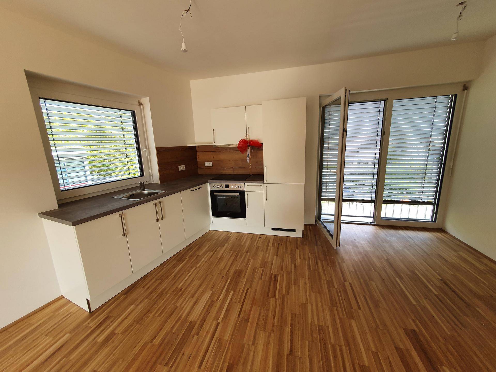 Moderne Einbauküche mit weißen Schränken, dunkler Arbeitsplatte, Parkettboden und Terrassenzugang.