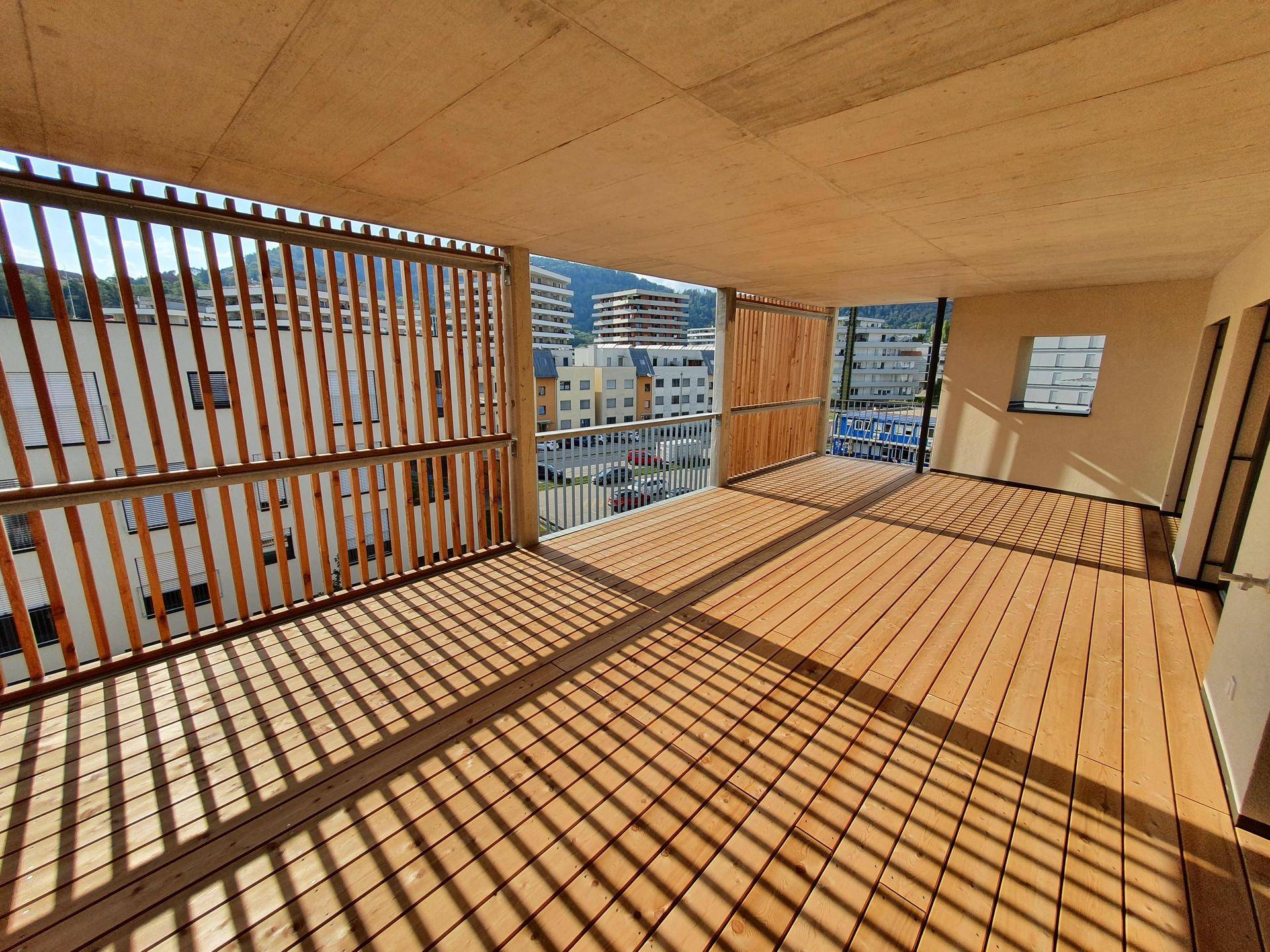 Große, sonnige Terrasse mit Holzboden und Holzlamellen, bietet einen weiten Blick auf die Stadt.