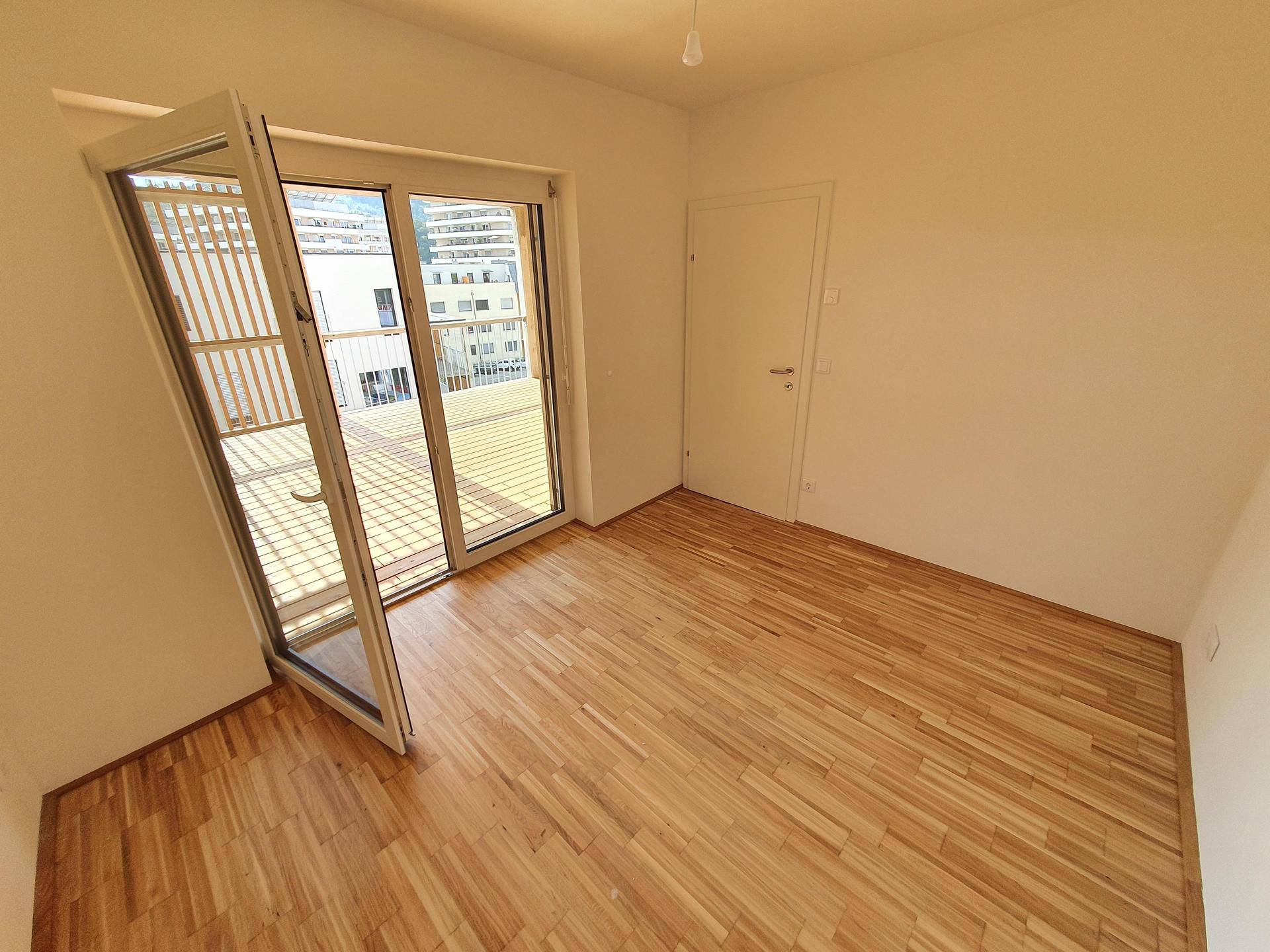 Helles Schlafzimmer mit Parkettboden und direktem Zugang zu einer sonnigen Außenterrasse.
