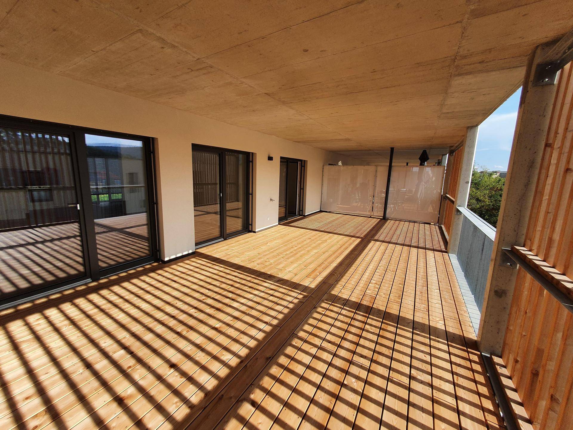 Weitläufige Terrasse mit Holzdielen und viel Sonnenlicht, umgeben von modernen Stadtgebäuden.