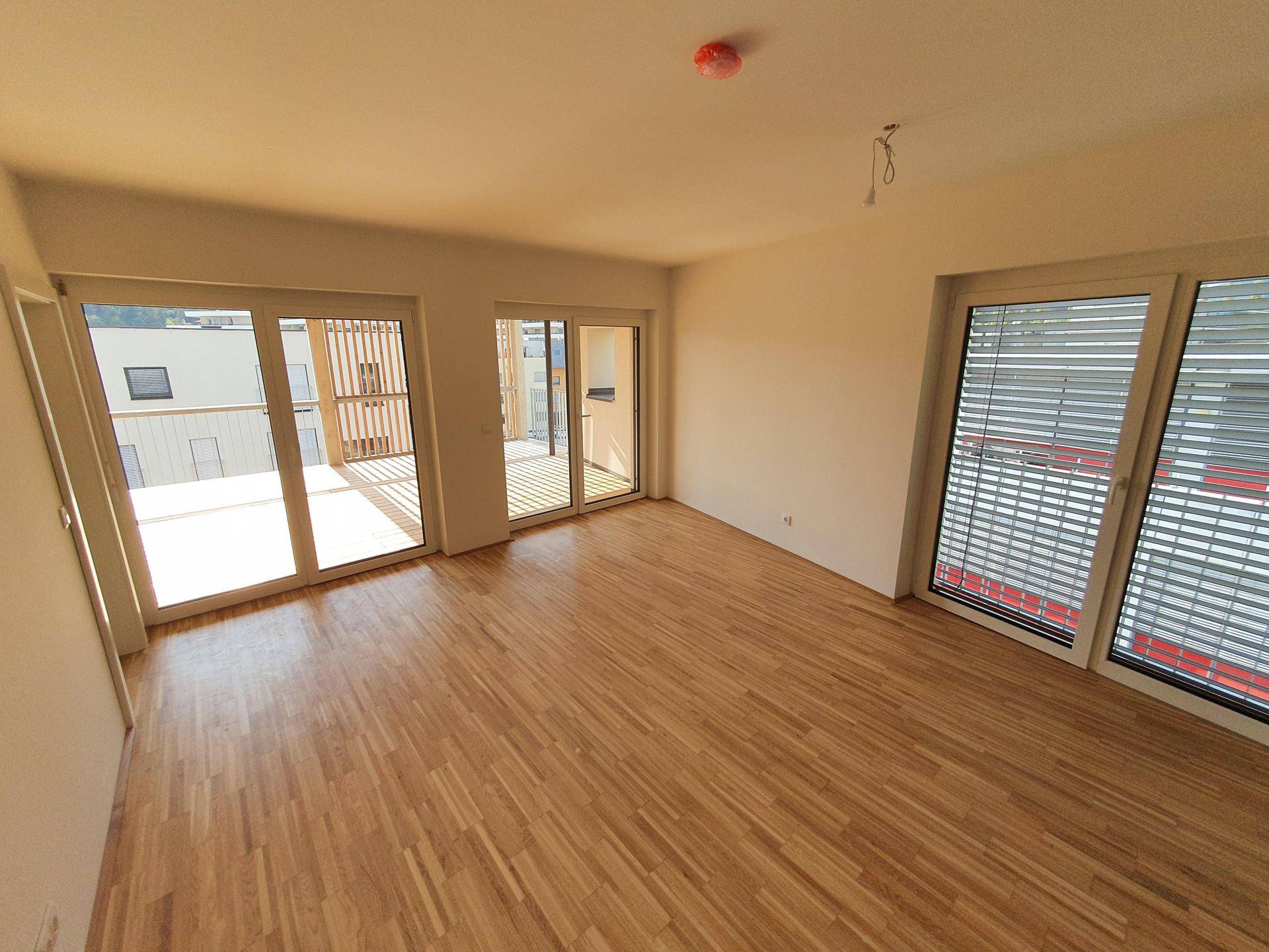 Geräumiges Wohnzimmer mit hellem Parkettboden und großen Schiebetüren, die zur Terrasse führen.