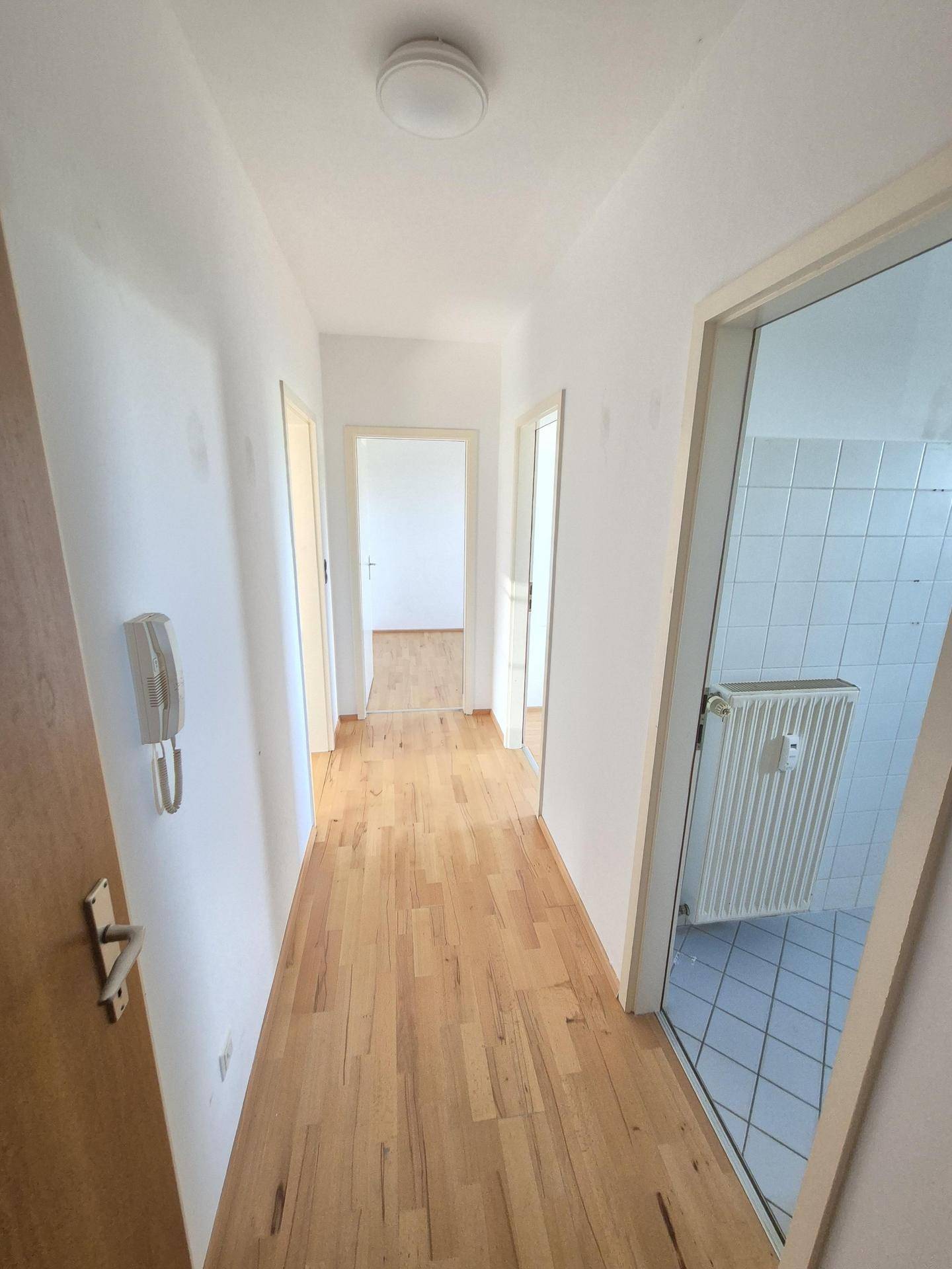 Langer Flur mit hellem Laminatboden, der zu verschiedenen Zimmern der Wohnung führt.