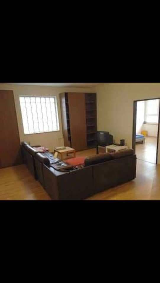 Geräumiges Wohnzimmer mit dunklen Sofas, Holzregalen und einem großen Fenster für natürliches Licht.