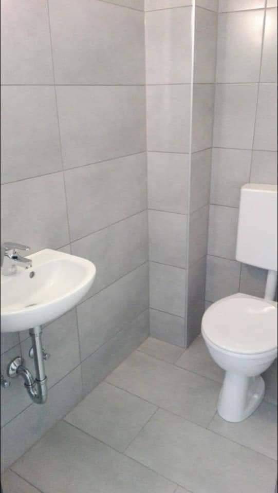 Modern gefliestes Gäste-WC mit wandmontierter Toilette und kleinem Waschbecken in hellem Grau.