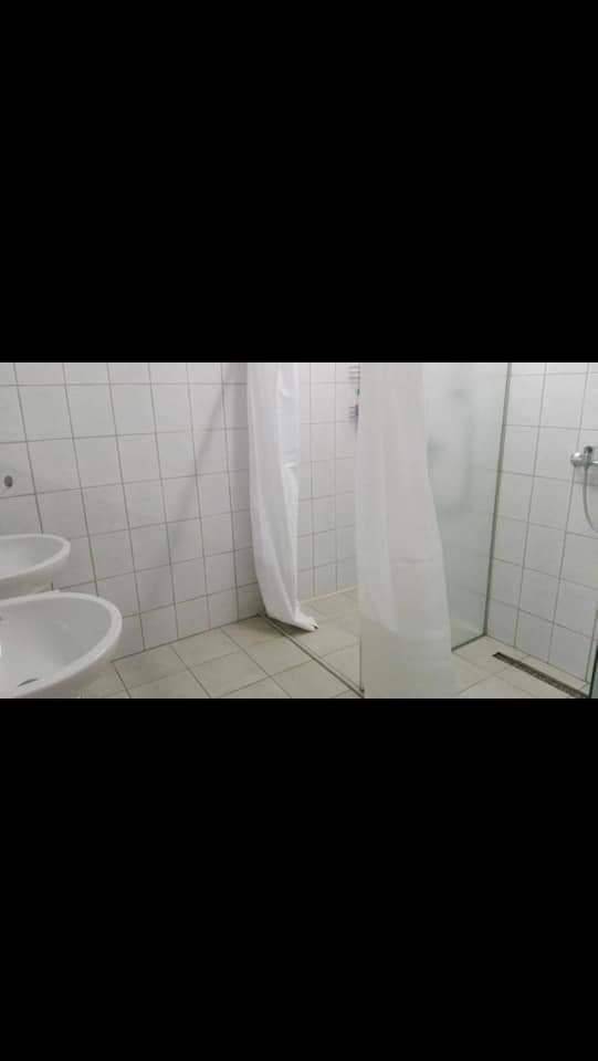 Badezimmer mit weißen Fliesen, zwei Waschbecken und einer Duschkabine mit Vorhang für Komfort.