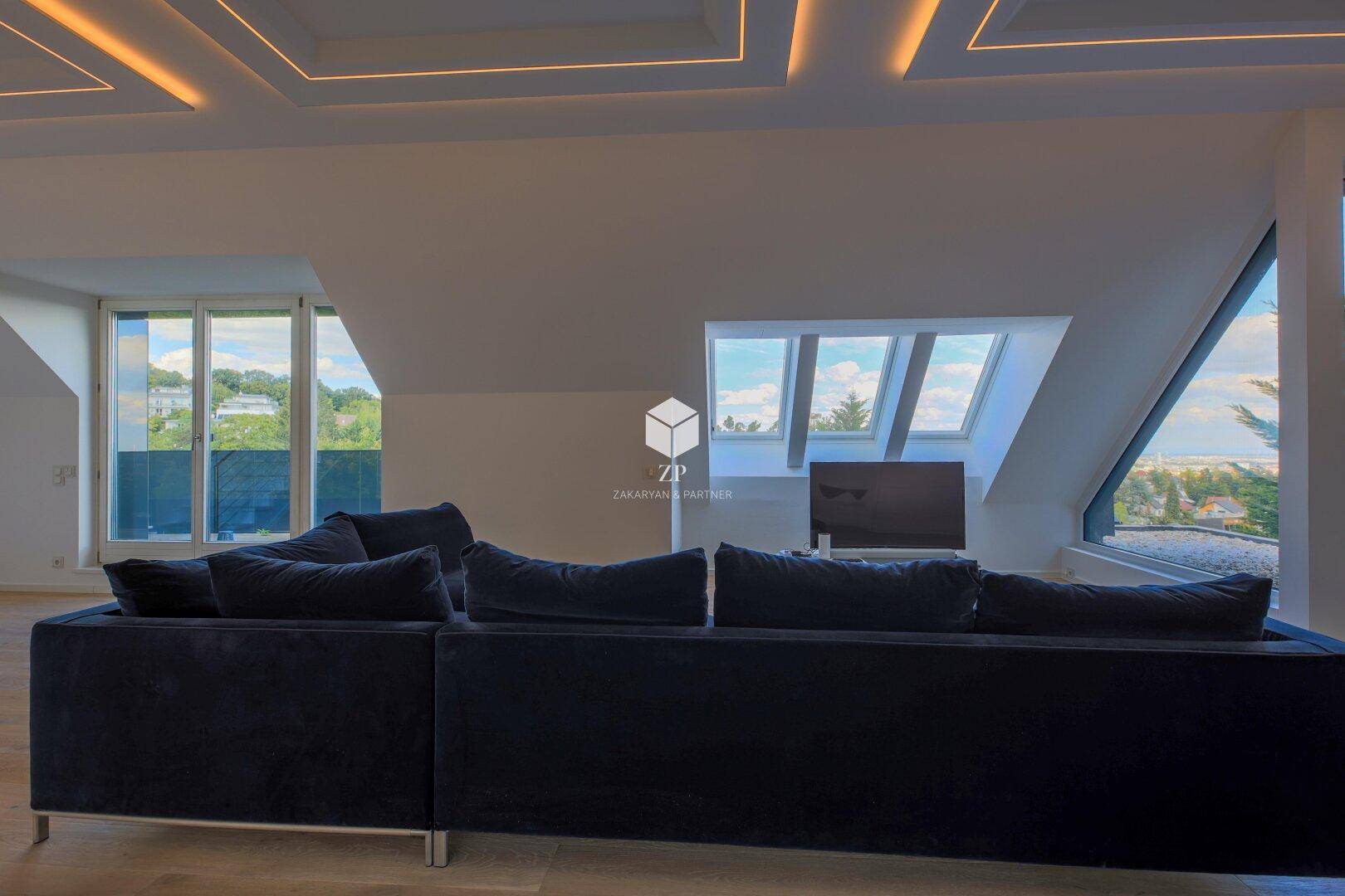 Gemütlicher Wohnbereich mit blauer Couch, großen Dachfenstern und weitem Blick ins Grüne.
