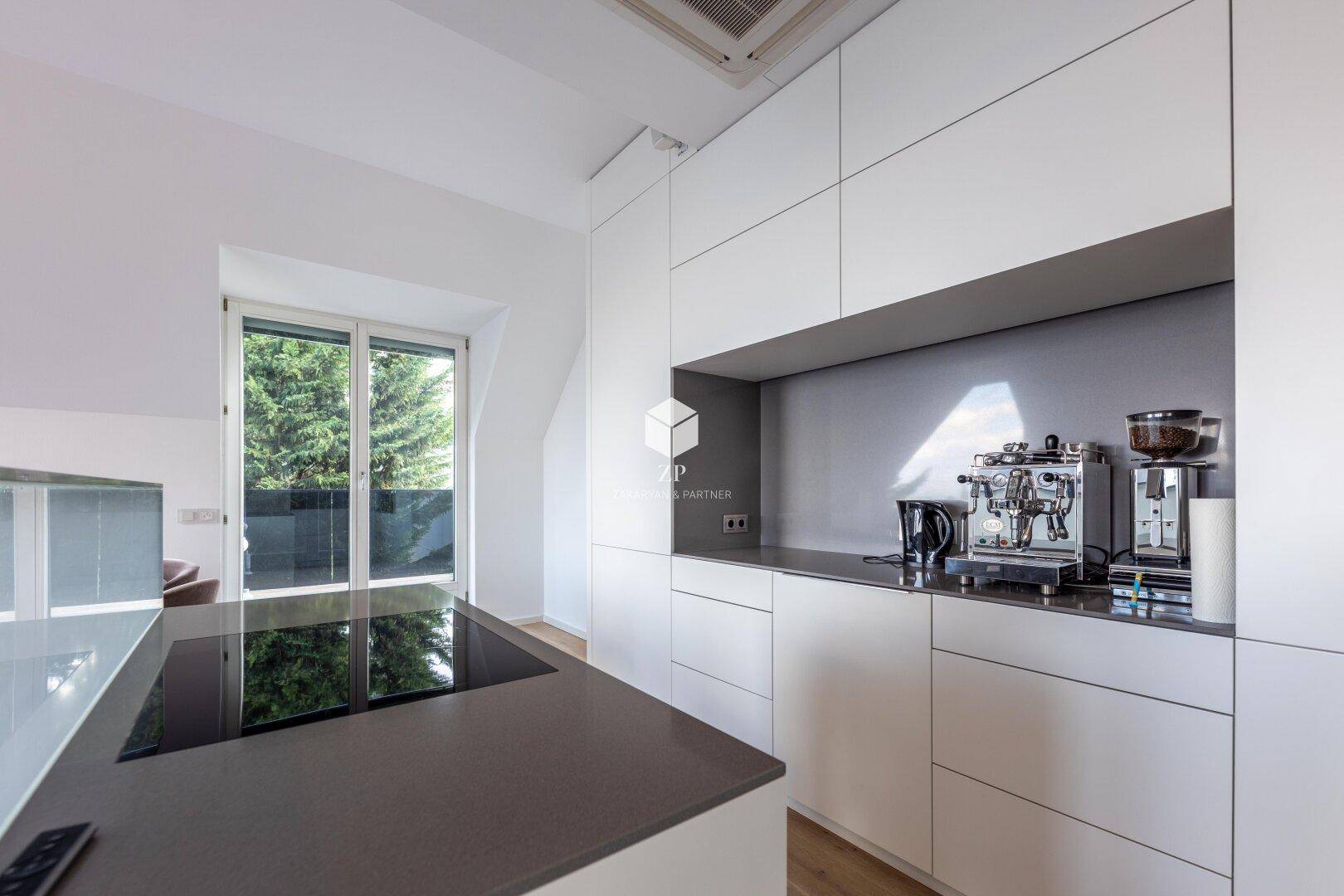 Helle Küche mit Induktionskochfeld, Kaffeemaschine und Fenster mit Blick ins Grüne.
