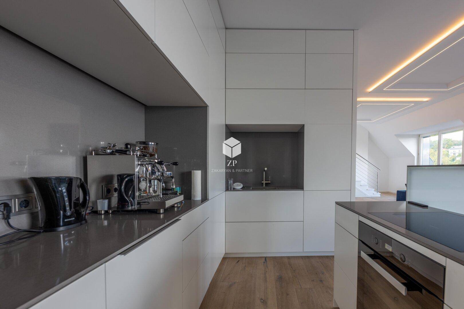 Moderne Einbauküche mit weißen Schränken, dunkler Arbeitsplatte und integrierter Spüle.