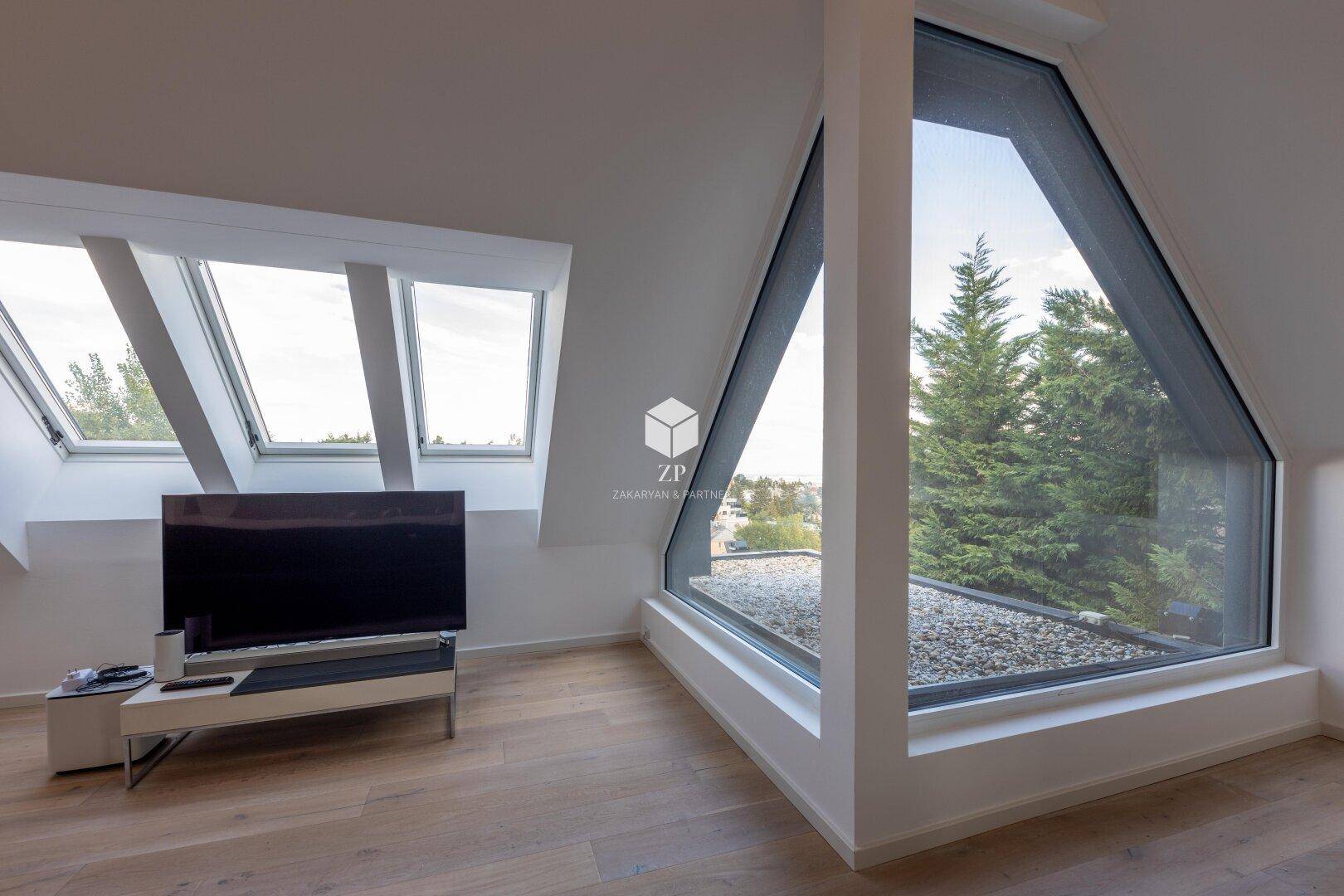Heller Wohnbereich mit großen, schrägen Fenstern und weitem Blick über die Baumwipfel.