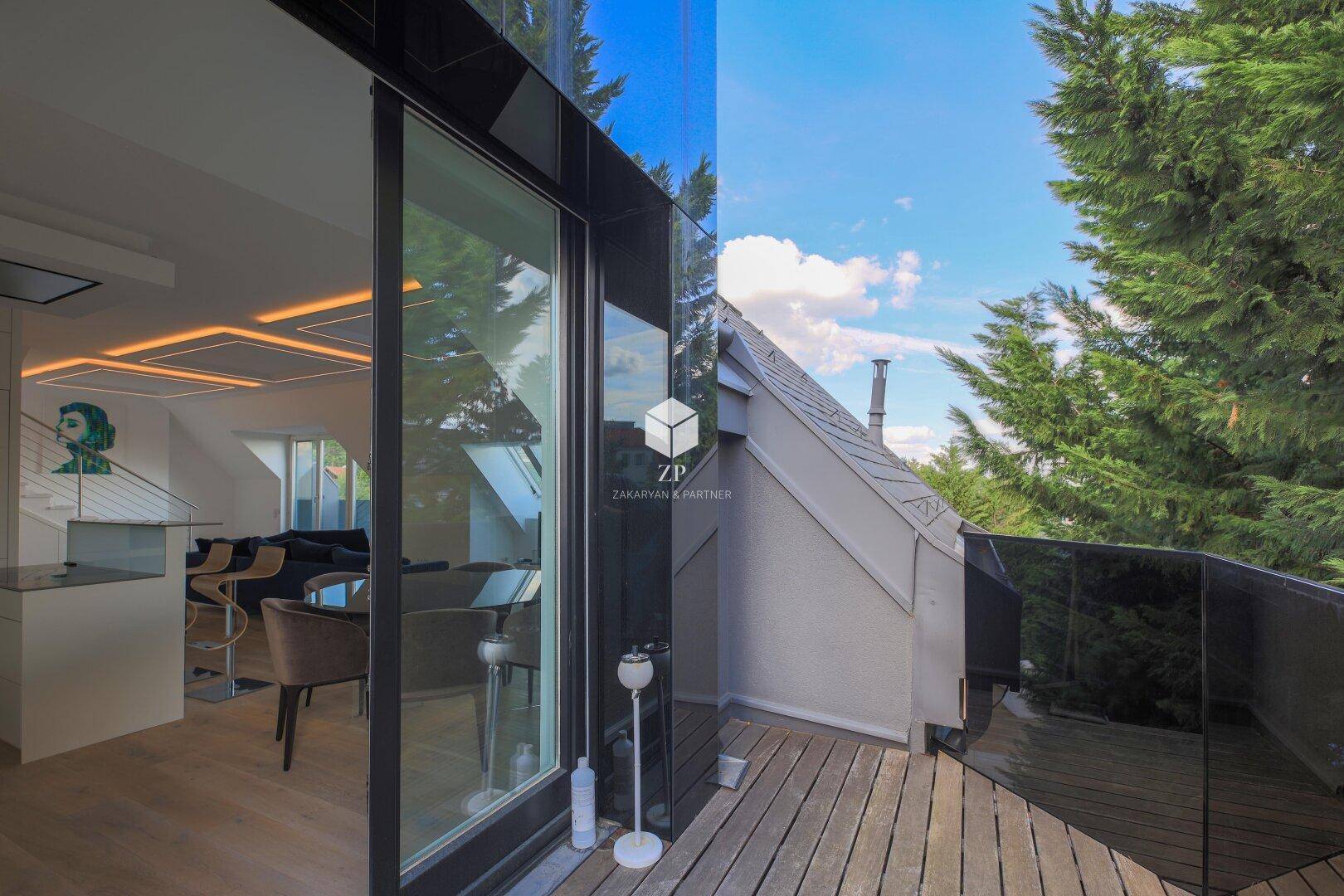 Moderner Balkon mit Glasgeländer und Holzboden, der einen Blick ins Grüne bietet.