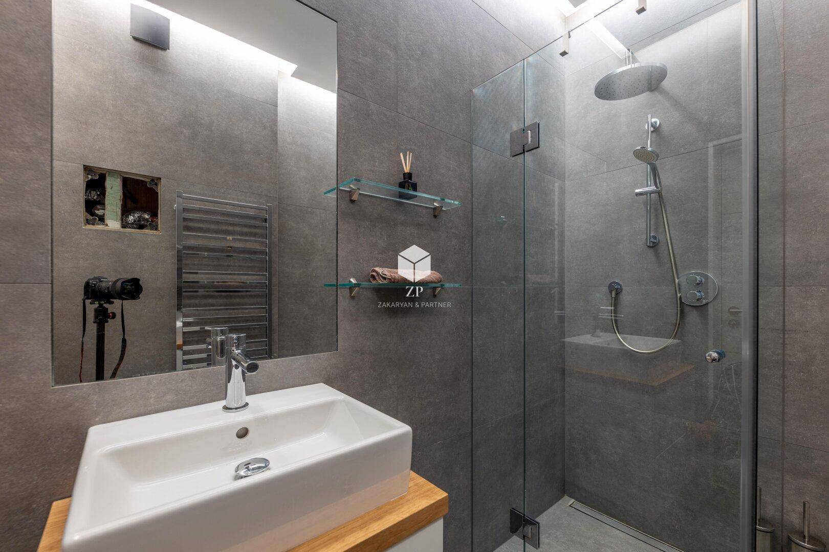 Modernes Badezimmer mit großer begehbarer Dusche, Einzelwaschbecken und grauen Fliesen.