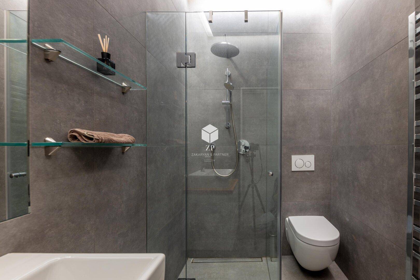 Zeitgemäßes Badezimmer mit bodengleicher Dusche, wandhängendem WC und grauen Fliesen.