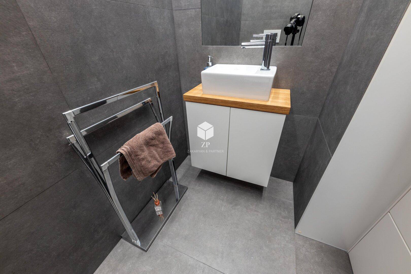 Kleines Badezimmer mit modernem Waschbecken, Holzplatte und Handtuchständer.