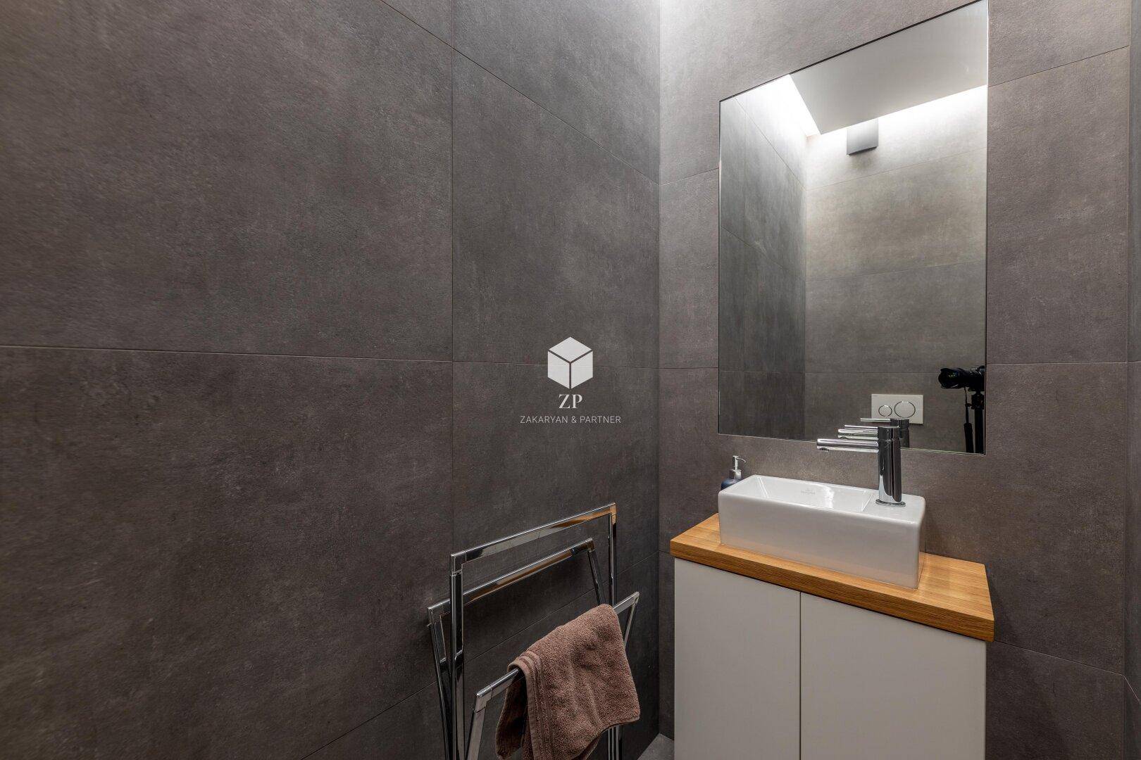 Modernes Badezimmer mit Waschbecken, großem Spiegel und grauen Fliesen.