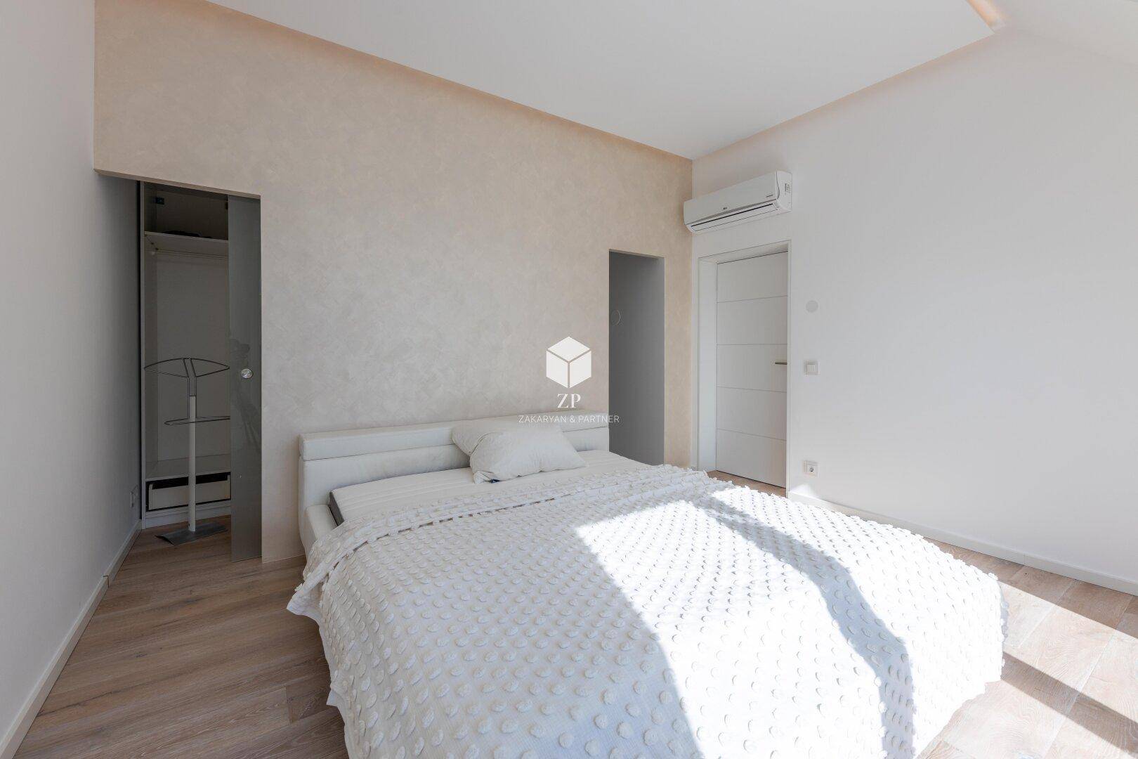 Helles Schlafzimmer mit Doppelbett, Holzboden und Zugang zu einem begehbaren Kleiderschrank.