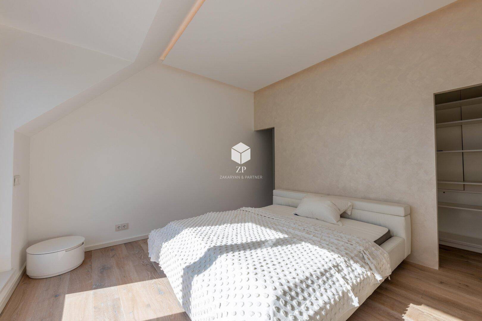 Schlafzimmer mit hellem Holzboden, Dachschräge und Zugang zum begehbaren Kleiderschrank.