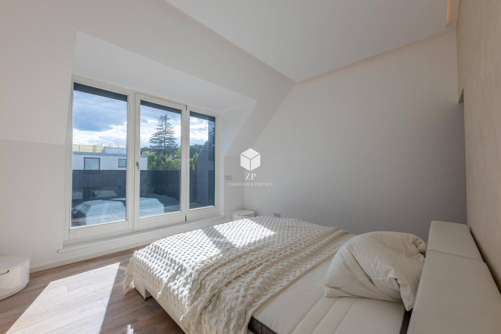 Schlafzimmer mit großem Fenster, das viel Tageslicht und einen Blick ins Grüne bietet.
