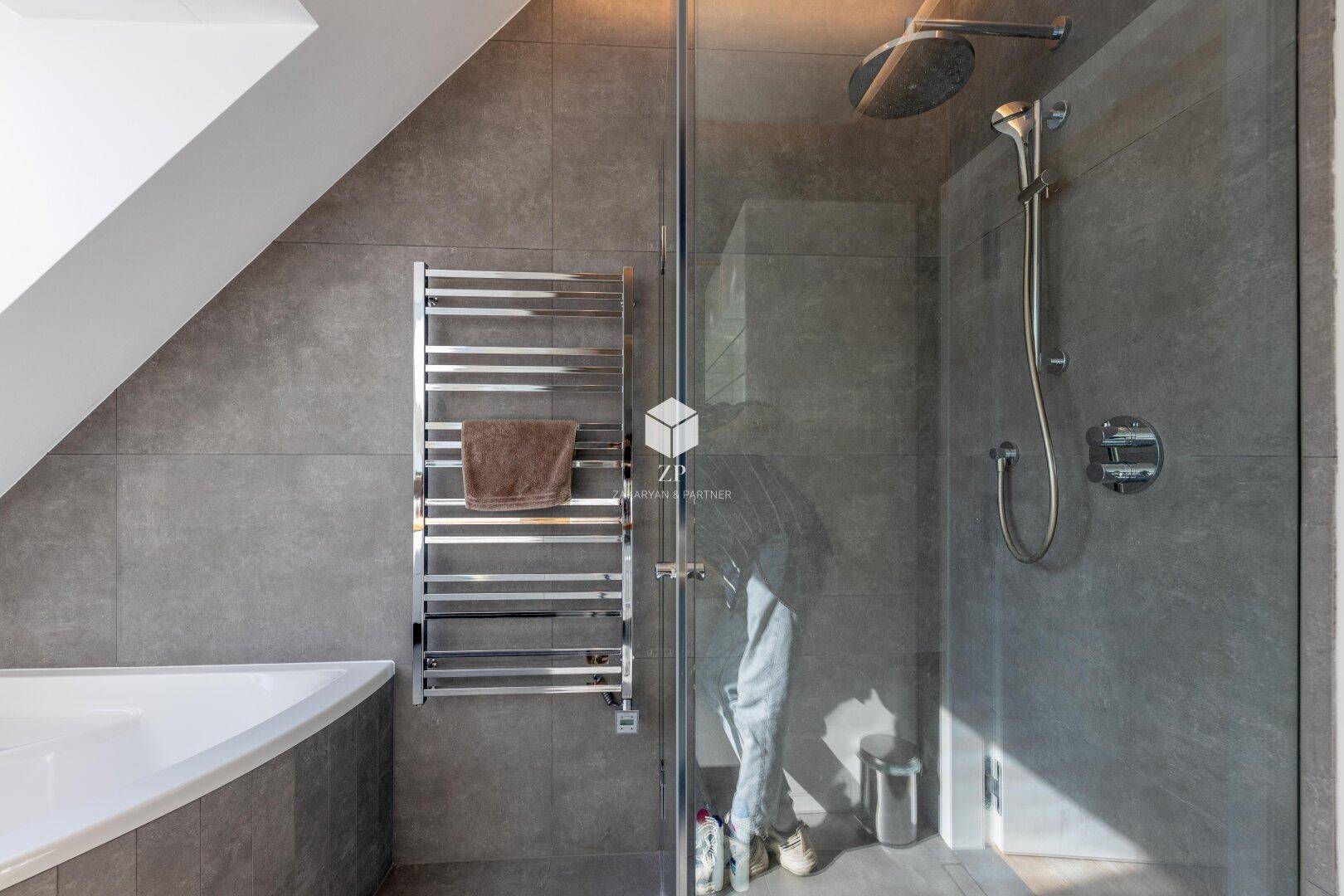 Zeitgemäßes Badezimmer mit großer Dusche, Badewanne und grauen Fliesen.