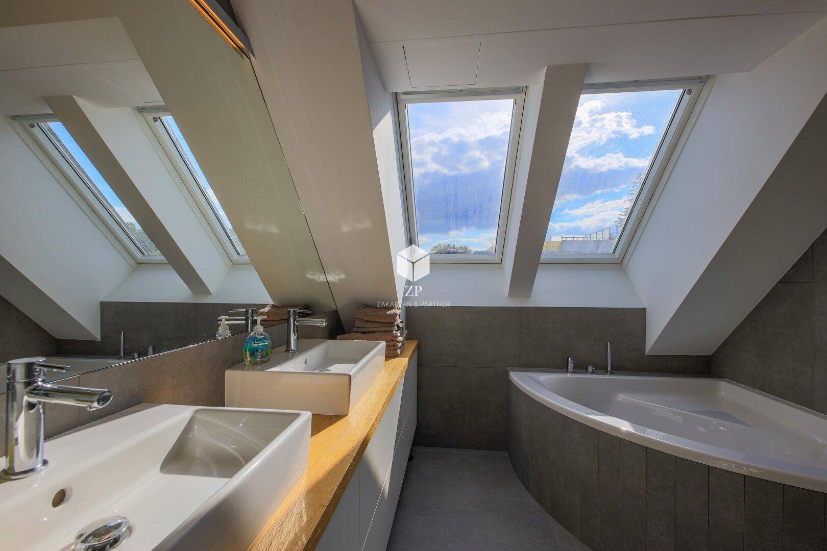 Lichtdurchflutetes Badezimmer mit Doppelwaschbecken, Badewanne und mehreren Dachfenstern.