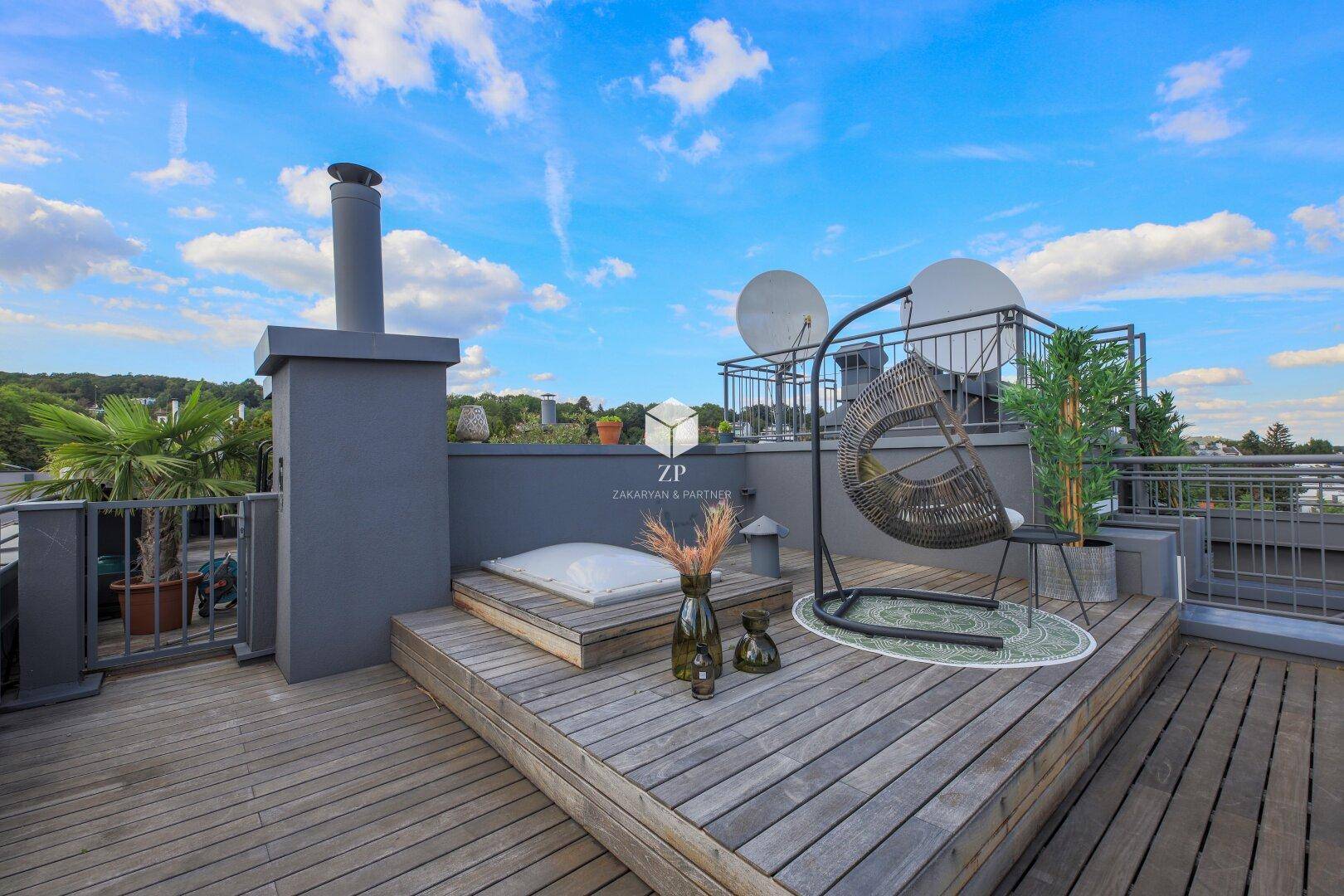 Entspannungsbereich auf der Dachterrasse mit Hängesessel und Holzboden unter blauem Himmel.