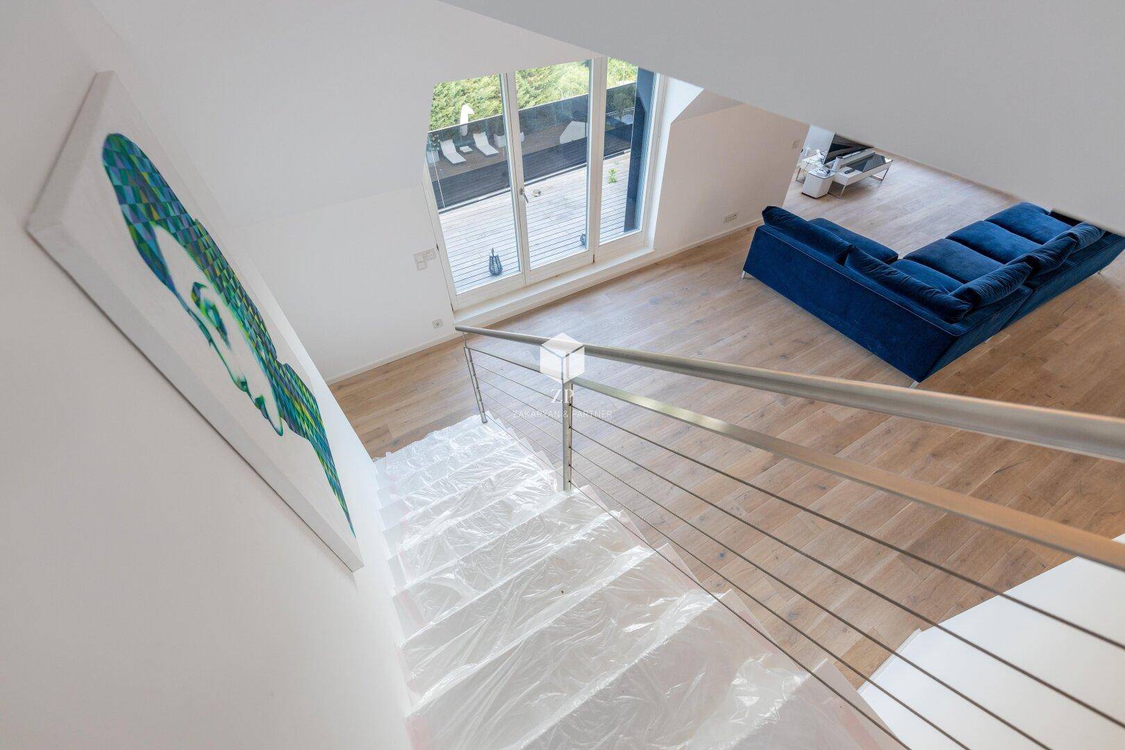 Blick von der Treppe in den offenen Wohnbereich mit blauer Couch und Zugang zur Terrasse.